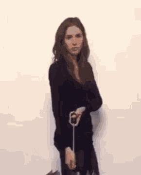 a woman in a black sweater is standing in front of a white wall holding a cell phone .