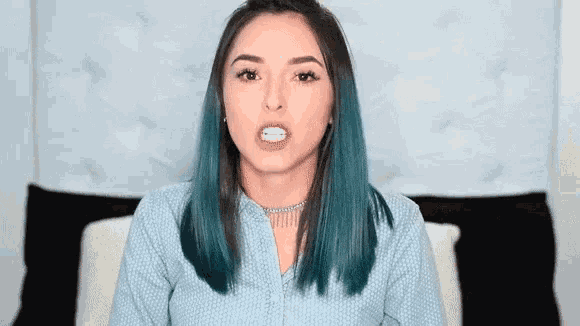 a woman with blue hair and a choker is making a funny face .