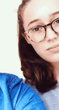 a woman wearing glasses and a blue shirt takes a selfie