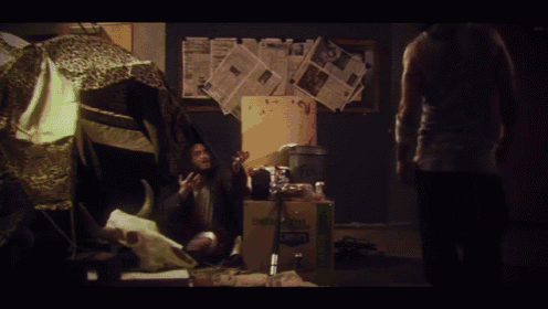 a man is standing in a room with newspapers on the wall and a box that says ' coca-cola ' on it