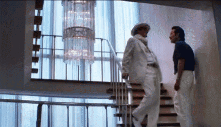 a man in a white suit is walking down a set of stairs next to another man .