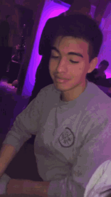 a young man wearing a gray shirt with a circle on it looks at the camera