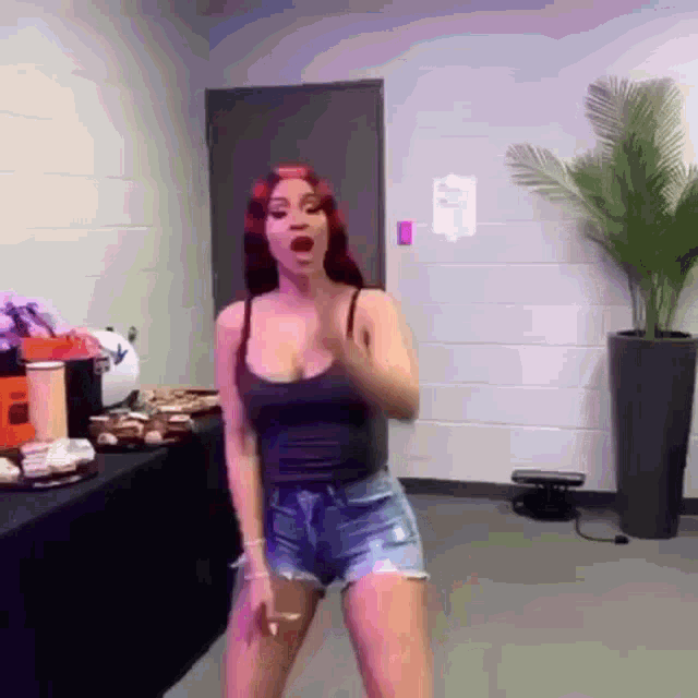 a woman in a black tank top and shorts is dancing in a room