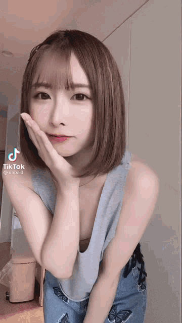 a woman in a gray tank top and blue jeans is making a tiktok