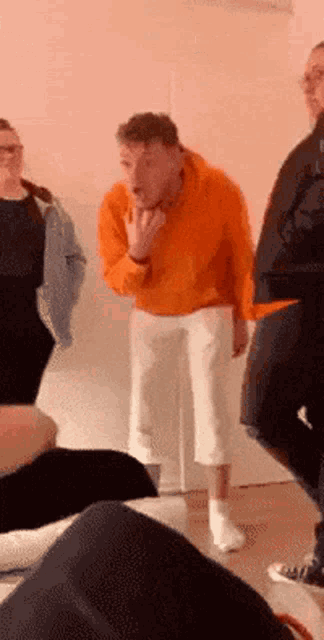 a man in an orange hoodie is standing in a room with a group of people