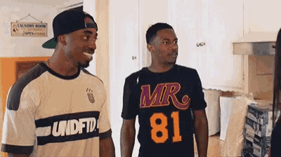 two men are standing next to each other in a kitchen and one of them is wearing a shirt that says mr 81 .