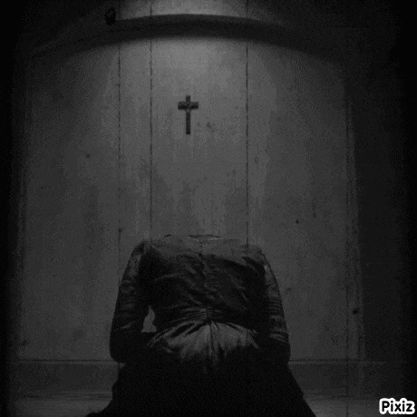 a black and white photo of a woman kneeling in front of a wall with a cross on it