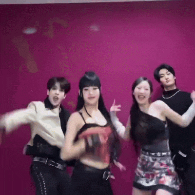 a group of people are standing next to each other in front of a pink wall and dancing .