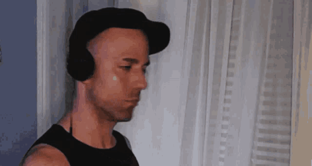 a man wearing headphones and a hat is standing in front of a window .