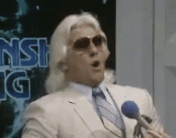 a man wearing sunglasses and a white suit is speaking into a microphone .