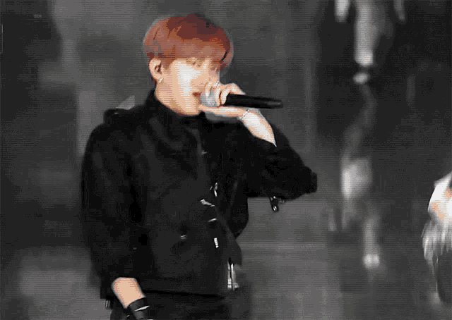 a man is singing into a microphone while wearing a black jacket .