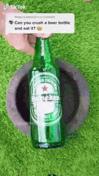 a green bottle of heineken beer is sitting in a hole in the grass .