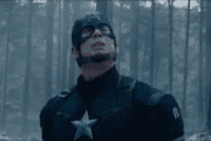 captain america is standing in the woods wearing a helmet and sunglasses .