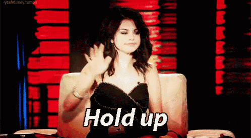 a woman in a black dress is sitting in a chair and waving her hand with the words hold up above her