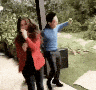 a man in a blue sweater is dancing with a woman in a red jacket .
