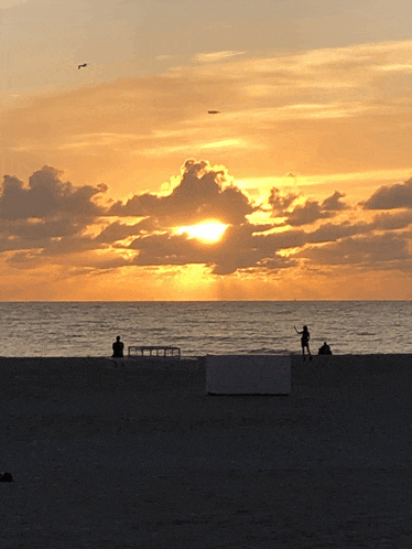 the sun is setting over the ocean and a person is flying a kite on the beach