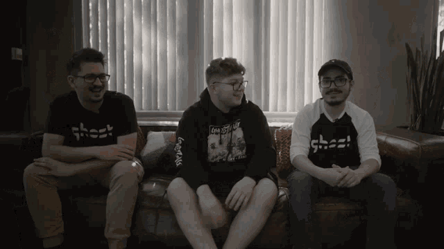 three men are sitting on a couch and one has a shirt that says ghost on it