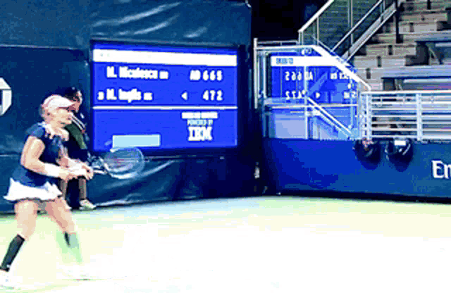 a woman is playing tennis in front of a scoreboard that says ibm on it