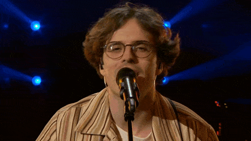 a man singing into a microphone with a man playing a piano in the background