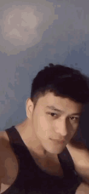 a young man wearing a black tank top is taking a selfie with a blue background .