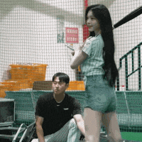 a woman is holding a bat while a man sits on a bench behind her .