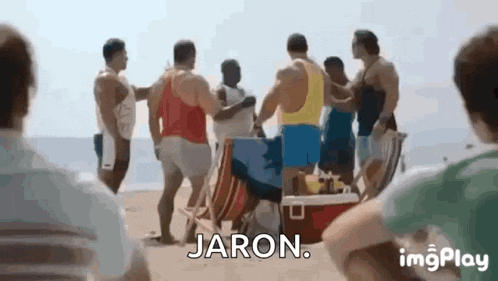 a group of men are standing on a beach talking to each other and jaron is standing in the middle of the group .