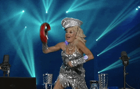 a woman in a silver dress is singing into a microphone and holding a tambourine