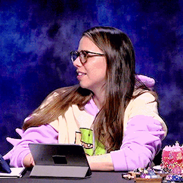 a woman wearing glasses is sitting at a desk using a tablet