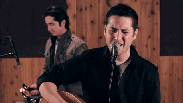 a man is singing into a microphone while another man plays a guitar