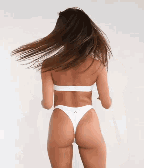 a woman in a white bikini is standing with her hair blowing in the wind .