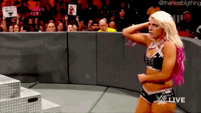 a female wrestler is standing in front of a crowd while wearing a pink top .