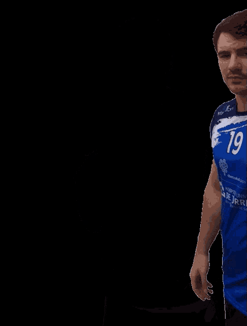 a man wearing a blue shirt with the number 19 on it stands with his hands on his hips
