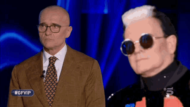 a man in a suit and tie stands next to another man in sunglasses with the hashtag #gfvip on the bottom