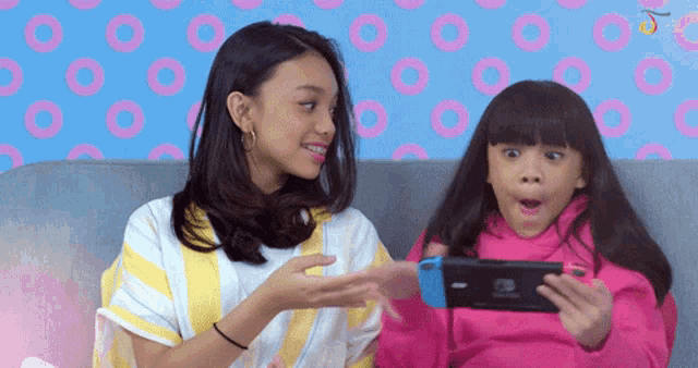 two girls are sitting on a couch and one is playing a video game