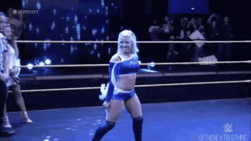 a woman in a blue outfit is standing in a wrestling ring with a crowd behind her .