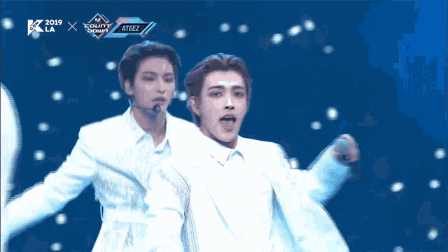 a man in a white suit stands on a stage in front of a sign that says ateez