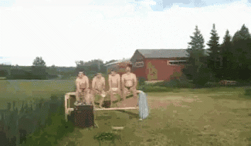 a group of naked men are sitting on a bench in a field near a lake .