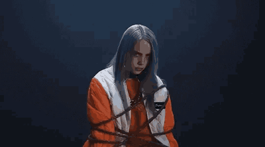 billie eilish is tied up with ropes in a dark room and looking at the camera .