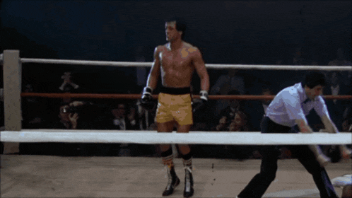 a man in yellow shorts stands in a boxing ring with a referee