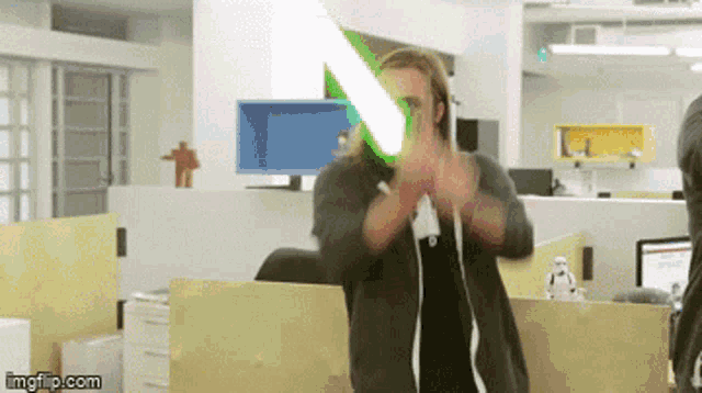 a man in an office is holding a green light saber in front of his face