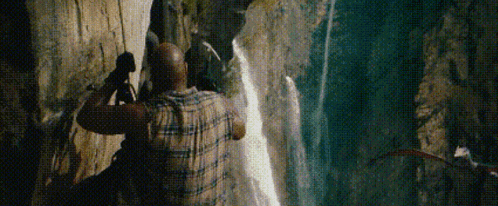 a man is standing in front of a waterfall in a canyon .