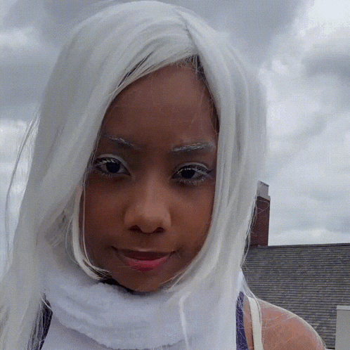 a woman wearing a white wig and a white scarf looks at the camera