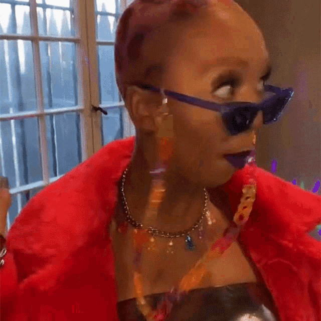 a woman wearing sunglasses and a red fur coat is looking at the camera .
