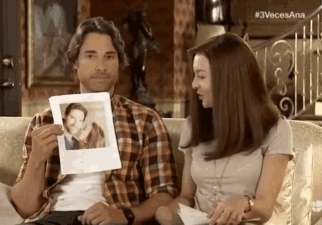 a man and woman are sitting on a couch looking at a picture of a man and woman .