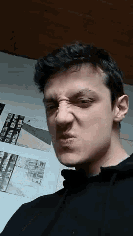 a young man is making a funny face in front of a wall with pictures on it