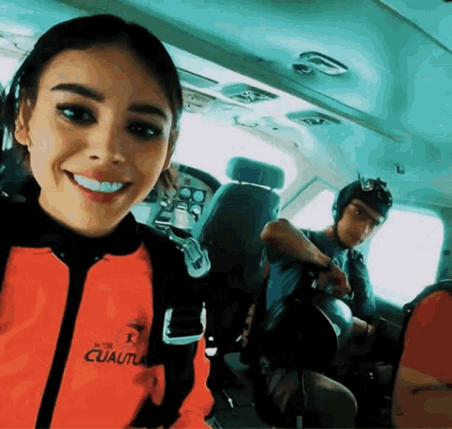 a woman wearing an orange jacket that says cuautia smiles for the camera