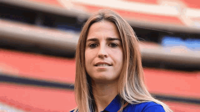 a woman in a blue shirt stands in front of a stadium