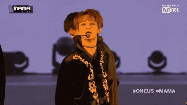 a man stands on a stage with a microphone in his mouth in front of a screen that says mama