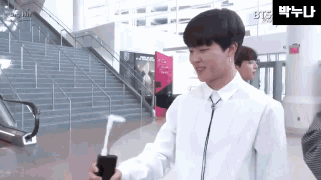 a young man in a white shirt is standing in front of an escalator and stairs holding a toothbrush