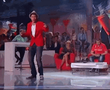 a man in a red jacket is dancing on a stage in front of a crowd